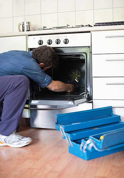 Homme qui répare l'intérieur d'un four, avec une boîte à outil posée sur le sol