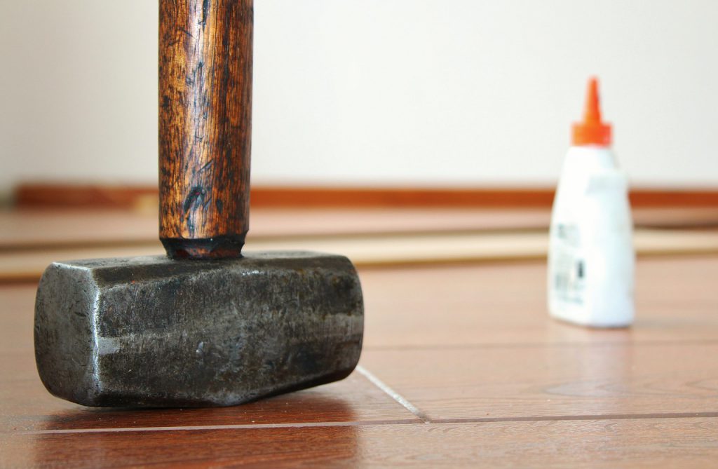 marteau posé sur du parquet avec un tube de colle polymère en arrière-plan